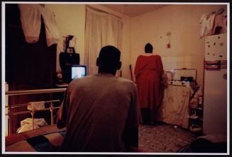 Couple vu de dos, femme avec robe rouge. Guillaume Collanges, "Hôtels meublés - Si tu ne paies pas, tu t’en vas", entre 2000 et 2001, tirages gélatino-argentiques couleur, 41 cm x 62 cm, Collection du Musée national de l'histoire de l'immigration. 2007.59.1