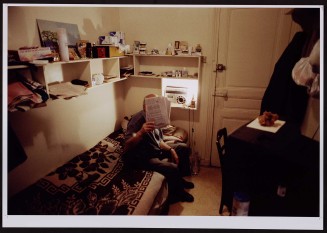  Locataire âgé cachant son visage derrière un journal. Guillaume Collanges, "Hôtels meublés - Si tu ne paies pas, tu t’en vas", entre 2000 et 2001, tirages gélatino-argentiques couleur, 41 cm x 62 cm, Collection du Musée national de l’histoire de l'immigration. 2007.59.10