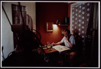 Locataire âgé assis à son bureau et fumant. Guillaume Collanges, "Hôtels meublés - Si tu ne paies pas, tu t’en vas", entre 2000 et 2001, tirages gélatino-argentiques couleur, 41 cm x 62 cm, Collection du Musée national de l’histoire de l'immigration. 2007.59.12