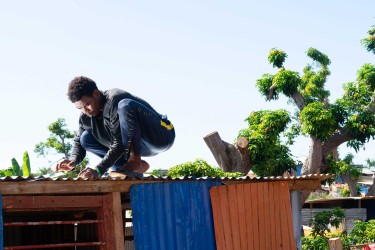 Laura Henno, "Un jeune cloue une tôle de son banga. Quartier informel de Barakani, Mayotte" © Laura Henno